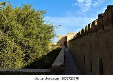Khasab Castle Courtyard interior wall detail with crenellated parapets.  Close up view of Khasab Castle interior courtyard wall detail with foliage and blue sky in the background in Khasab Oman.