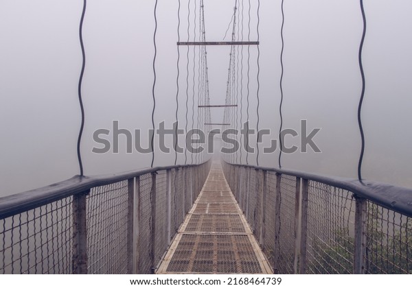 Khndzoresk suspension swinging bridge in fog.\
Suspension bridge over the gorge near Goris village. Early misty\
morning. Spooky\
atmosphere