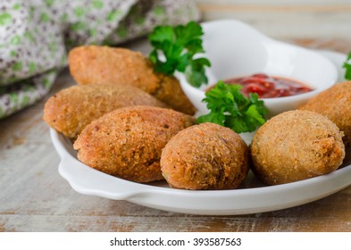 Kibbeh - traditional Arabian meatballs, minsed meat and bulgur or rice wheat fried snack with parsley, ketchup in white plate on wooden background. Eastern cuisine. Selective focus