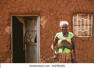 	KIBUYE, RWANDA, AFRICA - SEPTEMBER 11, 2015: Unknown woman. She looks into camera in front of her earthen house. Only her baby's feet appears. There is no glass on windows and doors of her house. 

