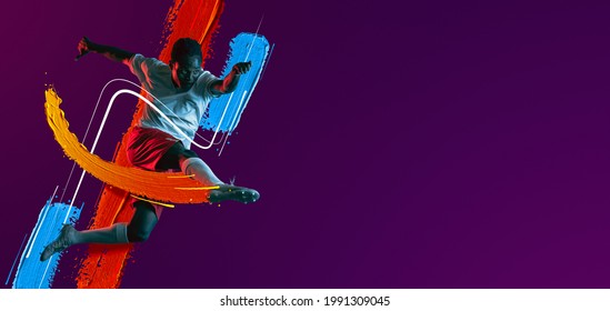 Kick In Jump. Portrait Of African Man, Male Soccer Football Player In White Red Uniform Isolated On Purple Neon Background. Concept Of Active Life, Team Game, Energy, Sport. Copy Space For Ad.