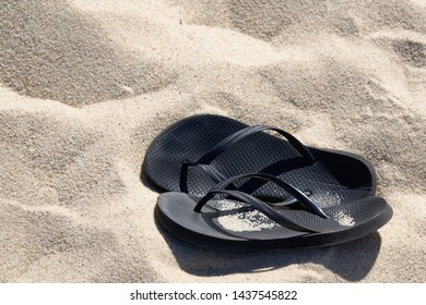 Kick Off Your Shoes And Enjoy The Summer On The Beach Concept With Black Flip Flop Sandals Laying In The Sand With Copy Space