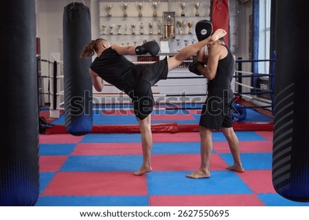 Kickboxer executing a high kick while coach holds pads during technique training session in the gym