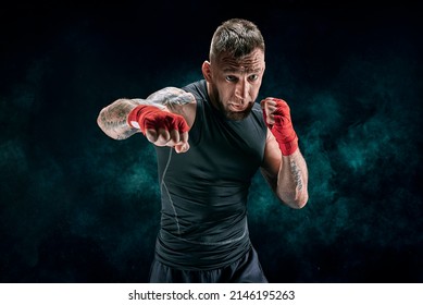 Kickboxer in red bandages is boxing against a background of smoke. The concept of mixed martial arts. MMA