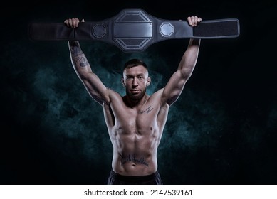 Kickboxer victoriously raises the belt won in the tournament against the backdrop of smoke. Sports competitions. Fight night. The concept of mixed martial arts. MMA