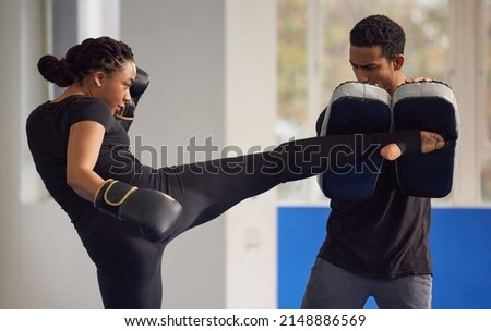 Kickboxing is the best form of dynamic exercise. Shot of a young woman practicing kickboxing with her trainer in a gym.