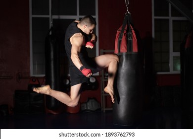 Kickboxing fighter Performing Jumping Air Kicks with Knee on Punch Bag. Caucasian Man Practicing Martial Arts Training at Urban Gym. High quality photo. - Powered by Shutterstock