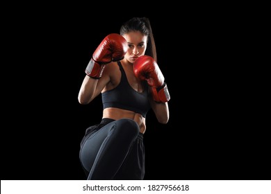 Kickboxing Woman In Activewear And Red Kickboxing Gloves On Black Background Performing A Martial Arts Kick. Sport Exercise, Fitness Workout.