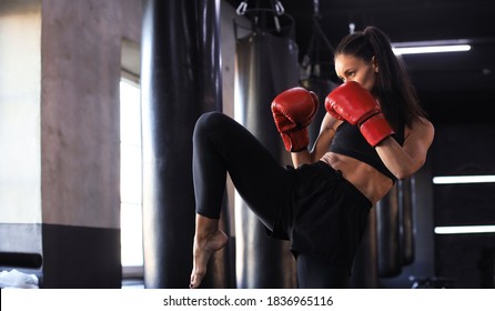 Mujer de Kickboxing en ropa activa y guantes de kickboxing rojo en fondo negro haciendo una patada de artes marciales. Ejercicio deportivo, ejercicio de fitness.