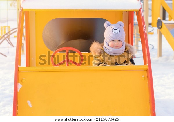 A kid 15-25 months old driving a toy car on a\
children\'s playground