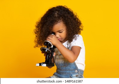 Kid African-american Girl Looking Through Microscope Over Yellow Studio Background