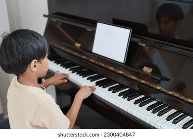 Kid asian black hair boy sitting and playing piano with tablet in living room house indoor. Musical and relaxation makes them happiness. Health care lifestyle concept. - Powered by Shutterstock