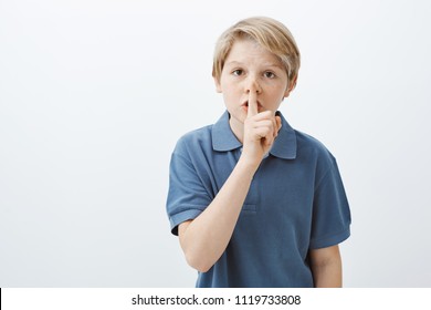 Kid Asking Friend Keep Secret. Portrait Of Serious Cute Blond Male Child In Blue T-shirt Saying Shh While Holding Index Finger Over Folded Lips, Making Shush Gesture, Worrying And Telling Stay Quiet