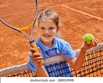 Kid athlete in blue form with racket and ball on  brown tennis court.
