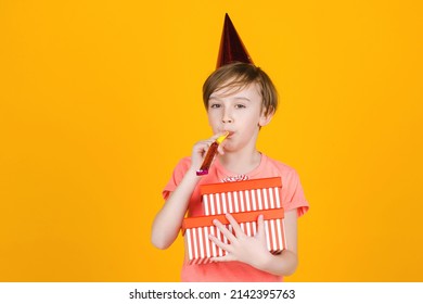 Kid with birthday gifts. Happy kid celebrating his ten year birthday. Child blowing whistle. Fun, joy, celebration and holiday. Cute boy with party hat isolated on yellow background.