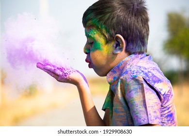 Kid blowing holi colour powder from hand during Holi festival celebration - Concept of young kids having fun by playing holi during festive