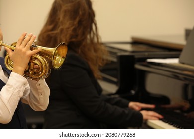 Kid Blowing A Musical Instrument Trumpet In A Music Lesson In The Classroom With A Person Playing The Piano.Concept Of Creativity And Education Of Children Background Image