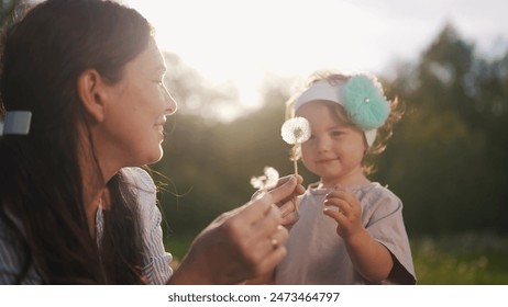 The Kid Blows Dandelion Family. happy family kid dream concept. The child blows dandelion. Mom teaches daughter toddler to blow on a dandelion flower, play lifestyle in park in summer - Powered by Shutterstock