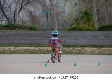 Kid With Blue Helmet In A Red Bike With Wheels In A Park