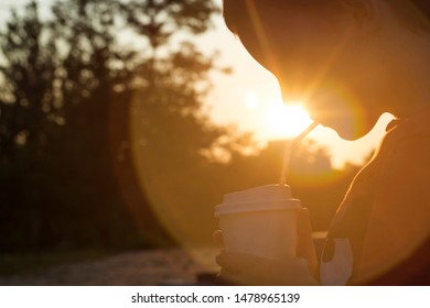 Kid Boy Drinks Cocoa Or Soda In A Cup With Tube On Sunset Background. Silhouette Of A Drinking Boy At Sunset.