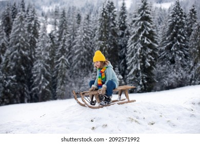 Kid Boy Enjoy A Sleigh Ride. Kid Sledding In Winter Snow Outdoor. Christmas Family Vacation. Child Boy Ride On A Wooden Retro Sleigh On A Sunny Winter Day On Winter Forest With Snow And Pine Trees.