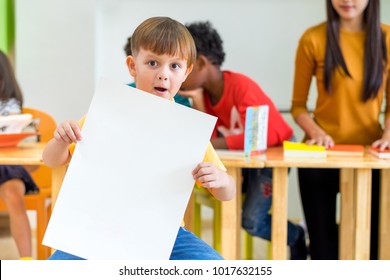 Kid Boy Holding Blank White Poster With Diversity Friends And Teacher At Background,Kindergarten School,mock Up Chalkboard For Adding Text.