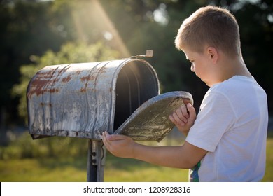 Kid Boy Opening A Post Box And Checking Mail. Kid Waiting For A Letter, Checking Correspondence And Looking Into The Metal Mailbox.