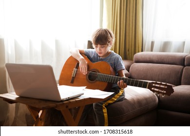 Kid  boy playing  guitar and watching  online lessons  on laptop while practicing at home.  Stay home. quarantine. Online training, online classes.
 - Shutterstock ID 1708315618