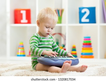 Kid boy plays toy piano sitting on floor in nursery