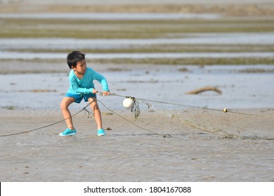 A Kid, Boy Is Pulling Worn, Unused Fishing Net Out Of The Beach In Thailand