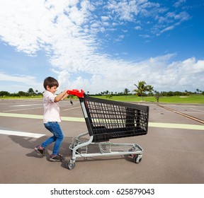 Kid Boy Pushing Empty Shopping Cart At Parking Lot