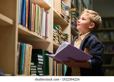 kid boy reading book between bookshelves in campus library, empty space. child is ready for school. education concept - Powered by Shutterstock