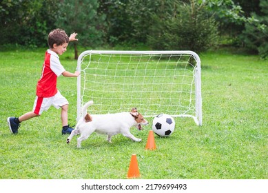 Kid Boy In Red And White Kit Playing Football (soccer) With His Dog At Training Ground