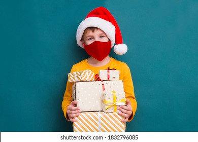 Kid Boy  In A Santa Hat Wearing Medical Face Mask  With Christmas Gift Boxes. Christmas Shopping.  Copy Space. New Normal.