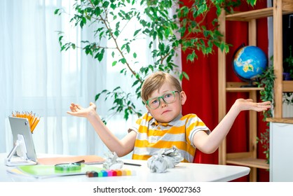 Kid Boy Sitting At Desk Clueless And Confused Expression With Arms And Hands Raised. Doubt Concept. I Don't Know. Mistake. Online School Lesson.