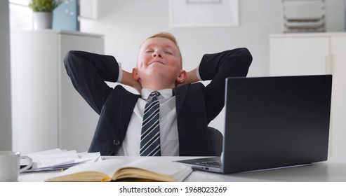Kid Businessman Working On Computer In Office. Successful And Happy Little Entrepreneur In Formal Wear Relaxing In Office Chair Working On Laptop