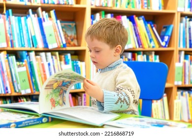 The Kid Carefully Examines The Pictures In Fairy-tale Books While Sitting In The Children's Library. Blurred Background