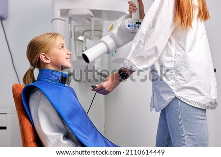 kid child girl patient is going to be done panoramic teeth x-ray in dental clinic, side view on caucasian child sitting on dental couch during taking x-ray picture process. health, medicine