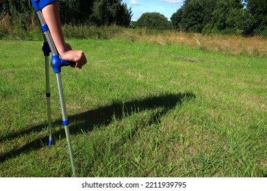 Kid With Crutches On A Green Lawn. Using Crutch To Walk After One Accident. Summer Time. Sweden, Europe.