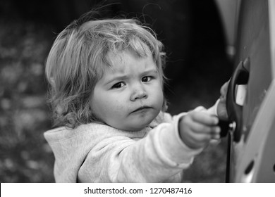 Kid Cute Fair-haired Blond Hazel-eyed Little Child Baby Boy Wearing Grey Hooded Coat Unlocking Car Door And Looking At Camera Portrait On Blurred Natural Background, Horizontal Picture