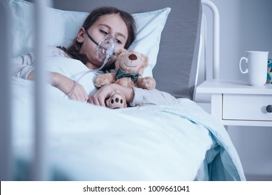 Kid With Cystic Fibrosis Lying In A Hospital Bed With Oxygen Mask And Plush Toy