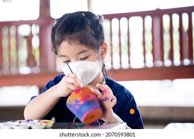 Kid doing art on plant pots made of terracotta clay. Child wearing white face mask.  - Powered by Shutterstock