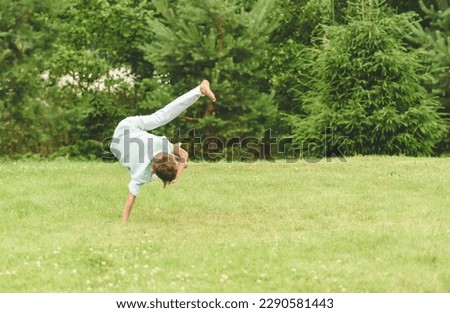 Kid doing martial art exercise training at home backyard lawn. Boy shows one hand handstand