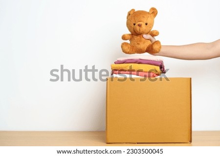 Kid Donation, Charity, Volunteer, Giving and Delivery Concept. Hand donate Bear doll and Clothes into cardboard box at home for support and help poor, refugee and homeless people. Copy space for text