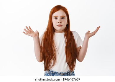 Kid Dont Know. Cute Redhead Little Girl Shrugging And Raise Hands Up, Look Clueless And Confused At Camera, Have No Idea, Cant Understand Something, Standing Over White Background