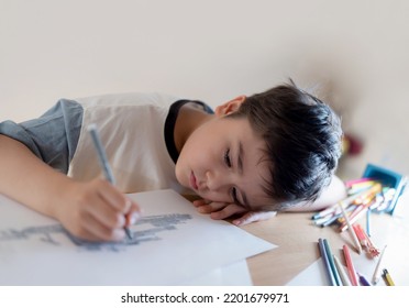 Kid Drawing On Paper, Portrait Boy Lying Head Down On Hand While Using Grey Pen Painting, Child With Thinking Face Doing Art And Craft For Homework.