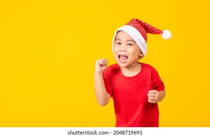 Kid Dressed In Red Santa Claus Hat, Portrait Of Asian Little Cute Boy Smile And Excited The Concept Of Holiday Christmas Xmas Day Or Happy New Year, Studio Shot Isolated On Yellow Background