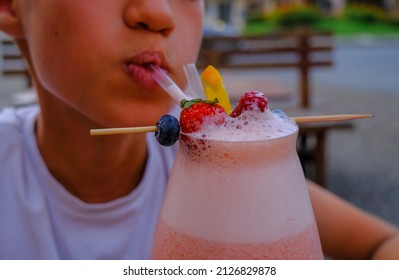  Kid Drinking Strawberry Smoothie With A Straw And Different Berries As A Decor Close-up. Healthy Food. Healthy Lifestyle.