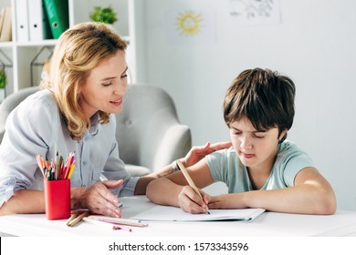 Kid With Dyslexia Drawing With Pencil And Child Psychologist Looking At It 