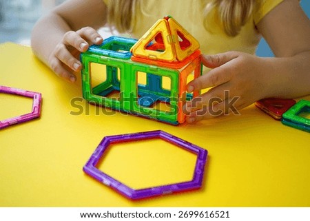 A kid experiments with spatial design using a magnetic constructor featuring colorful geometric tiles of various shapes and sizes.